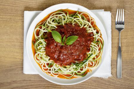 zucchini pasta with tomato sauce in white plate on wooden tableの写真素材