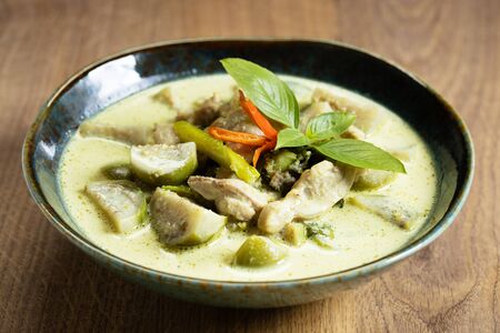 Thai chicken green curry, spicy coconut soup, with eggplant on wooden tableの写真素材