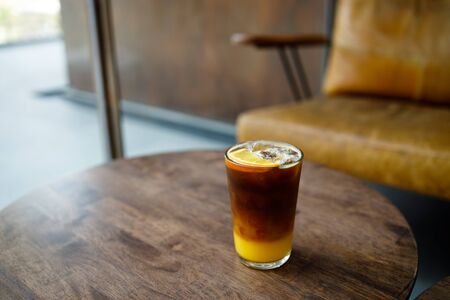 A glass of iced coffee with orange juice on wooden tableの写真素材