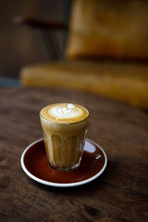 small cup of coffee with heart pattern froth on wooden table in cafe atmosphereの写真素材