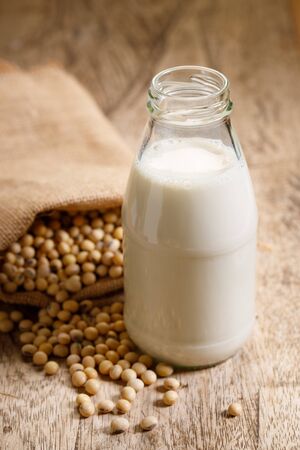 Soy beans in gunny bag and soy milk in glass bottle on old wooden tableの写真素材