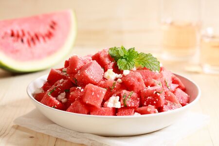 Watermelon salad with feta cheese and mint leaves in white bowl on wooden tableの写真素材