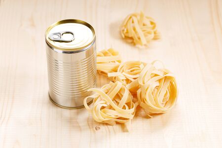 Dried Italian pasta fettuccine with canned sauce on wooden background, non-perishable food concept.の写真素材