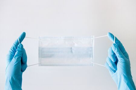 Hands of a medic in the blue latex gloves holding medical mask on whiteの写真素材