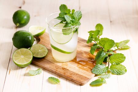 Lemonade or mojito cocktail with fresh lime and mint leaves, cold refreshing drink with ice on wooden table.の写真素材