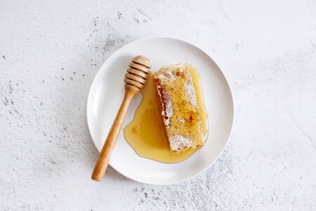 Sweet honeycomb and wooden honey dipper in white dish on marble backgroundの写真素材