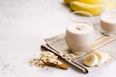 Vegan banana and oatmeal smoothie in a glass on white marble background. Healthy food concept.の写真素材