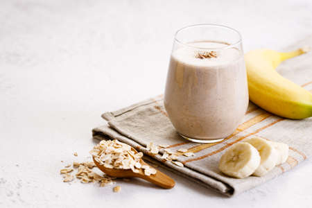 Vegan banana and oatmeal smoothie in a glass on white marble background. Healthy food concept.の写真素材
