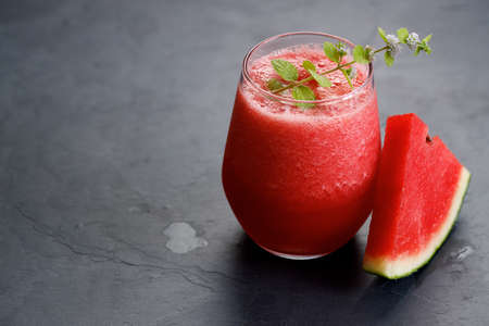 Glass of healthy watermelon smoothie with mint leaves on dark backgroundの写真素材