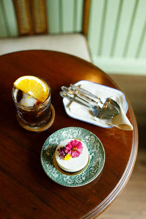 Piece of cake with edible flower and iced coffee on wooden table in small cafe. Coffee and cake.の写真素材