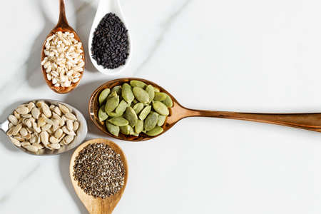 Various seeds with sesame, sunflower seeds, pumpkin seeds, chia and barley in spoons on a white...