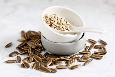Nutritious sunflower seeds in a white bowl, with a white ceramics spoonの写真素材
