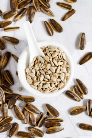 Nutritious sunflower seeds in a white bowl, with a white ceramics spoonの写真素材