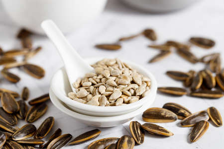Nutritious sunflower seeds in a white bowl, with a white ceramics spoonの写真素材