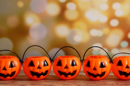 Five Halloween pumpkins with painted face on wooden table arranged against bokeh lights. Halloween background with copy space.の写真素材