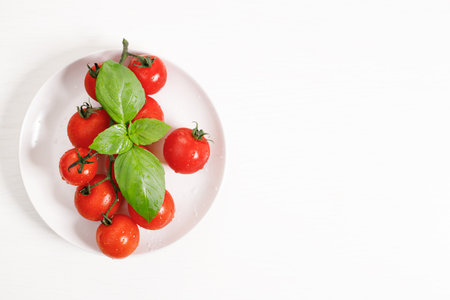fresh red tomatoes with basil on white wooden table. Vegetable tomato cooking concept. Top view.の写真素材
