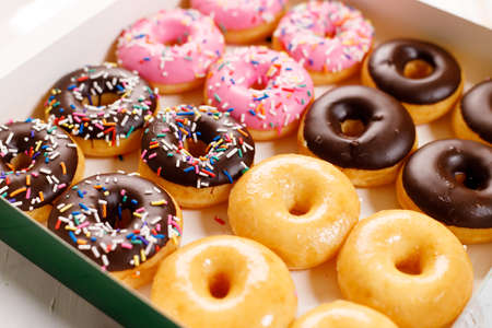 donuts with chocolate frosted, pink glazed and sprinkles in paper box, closeupの写真素材