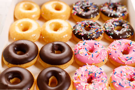 donuts with chocolate frosted, pink glazed and sprinkles in paper box, closeupの写真素材