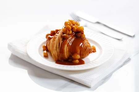 Fresh baked croissant with caramel sauce and Macadamia nut on white plateの写真素材