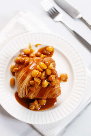 Fresh baked croissant with caramel sauce and Macadamia nut on white plateの写真素材