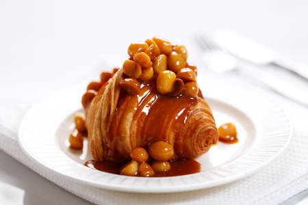Fresh baked croissant with caramel sauce and Macadamia nut on white plateの写真素材