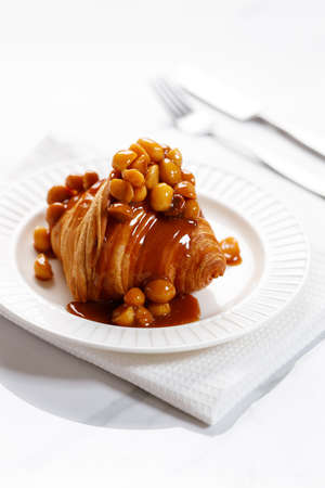 Fresh baked croissant with caramel sauce and Macadamia nut on white plateの写真素材