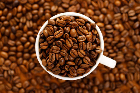coffee beans roasted in a coffee cup on coffee beans background, top viewの写真素材