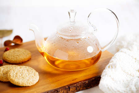 hot glass teapot with teabag and some herbal ingredients on wooden table background.の写真素材