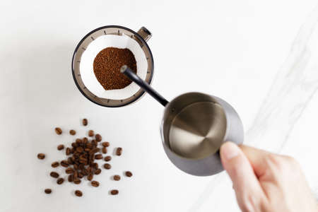 Barista hand holding coffee equipment, kettle, dripper over white table.の写真素材