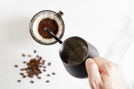 Barista hand holding coffee equipment, kettle, dripper over white table.の写真素材