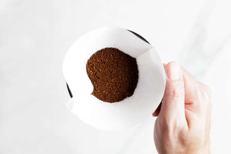 Barista hand holding coffee equipment, kettle, dripper over white table.
