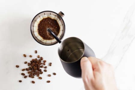 Barista hand holding coffee equipment, kettle, dripper over white table.の写真素材