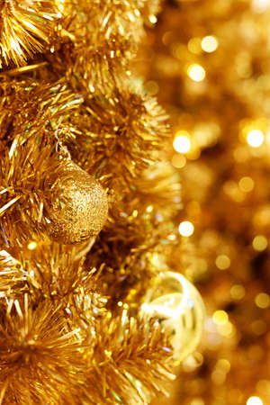 Beautiful Christmas and New years background with gold ornaments hanging on gold Christmas tree against a defocused lights background.の写真素材