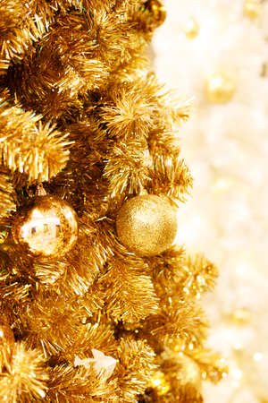 Beautiful Christmas and New years background with gold ornaments hanging on gold Christmas tree against a defocused lights background.の写真素材
