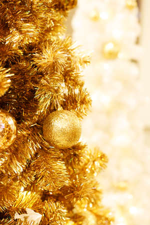 Beautiful Christmas and New years background with gold ornaments hanging on gold Christmas tree against a defocused lights background.の写真素材