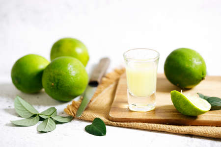 Lime juice and fresh green limes on white marble background. Closeup.の写真素材