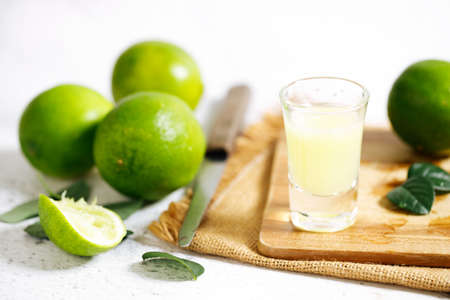 Lime juice and fresh green limes on white marble background. Closeup.の写真素材