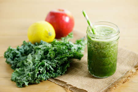 Healthy Green Smoothies of kale, apple and lemon in a glass with green straw on wooden table. Healthy vegetarian food concept.の写真素材