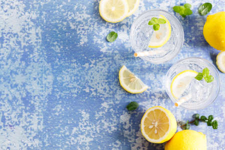 Lemonade iced drink with fresh mint leaves and fresh lemon slices . Cold refreshing drink or beverage with ice on white blue marble background.Top view with copy space.の写真素材
