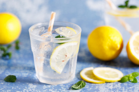 Lemonade iced drink with fresh mint leaves and fresh lemon slices . Cold refreshing drink or beverage with ice on white blue marble background.の写真素材