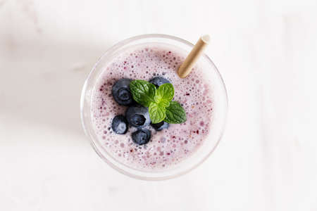 Tasty blueberry smoothie in a glass with pepper straw on white wooden table. Healthy refreshing drink concept.の写真素材