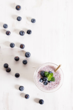 Tasty blueberry smoothie in a glass with pepper straw on white wooden table. Healthy refreshing drink concept.の写真素材