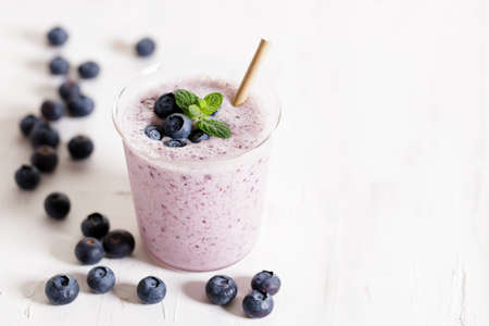 Tasty blueberry smoothie in a glass with pepper straw on white wooden table. Healthy refreshing drink concept.の写真素材