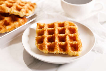 Croffle or Croisant waffle dessert, a marriage between a croissant and a waffle iron. Fresh baked croffle on a white plate. closeup.の写真素材