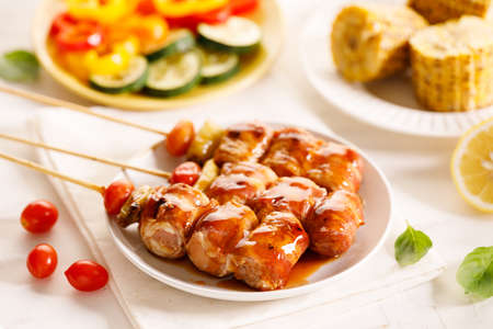 Grilled bacon and vegetable Skewers with bell peppers, zucchini, and tomatoes on white wooden background. Summer BBQ food concept.の写真素材