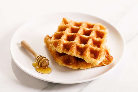 Croffle or Croisant waffle dessert, a marriage between a croissant and a waffle iron. Fresh baked croffle on a white plate. closeup.の写真素材