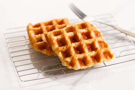 Croffle or Croisant waffle dessert, a marriage between a croissant and a waffle iron. Fresh baked croffle on a white plate. closeup.の写真素材