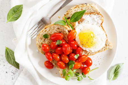 Healthy breakfast toast with fried egg, tomato salad and fresh basil on white plate.の写真素材