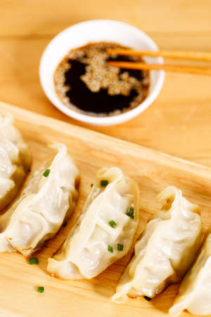 plate of gyoza dumplings with soy sauce and wooden chopstick on wooden table background. Asian food Gyoza or Jiaozi fried dumplings. Selective focus.の写真素材