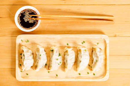 plate of gyoza dumplings with soy sauce and wooden chopstick on wooden table background. Asian food Gyoza or Jiaozi fried dumplings. Selective focus.の写真素材